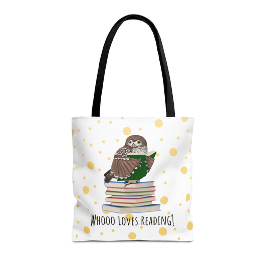 A white tote bag with black handles, decorated with a central illustration of a brown owl perched on a stack of books reading a green book. The bag has a white background with scattered gold polka dots and the text 'WHOOO LOVES READING!' printed below the illustration.