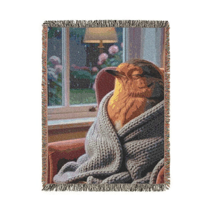 A rectangular woven throw blanket with fringed edges, featuring a printed scene of a robin bird wrapped in a gray knit blanket in front of a window. The blanket is shown upside down on a plain white background.