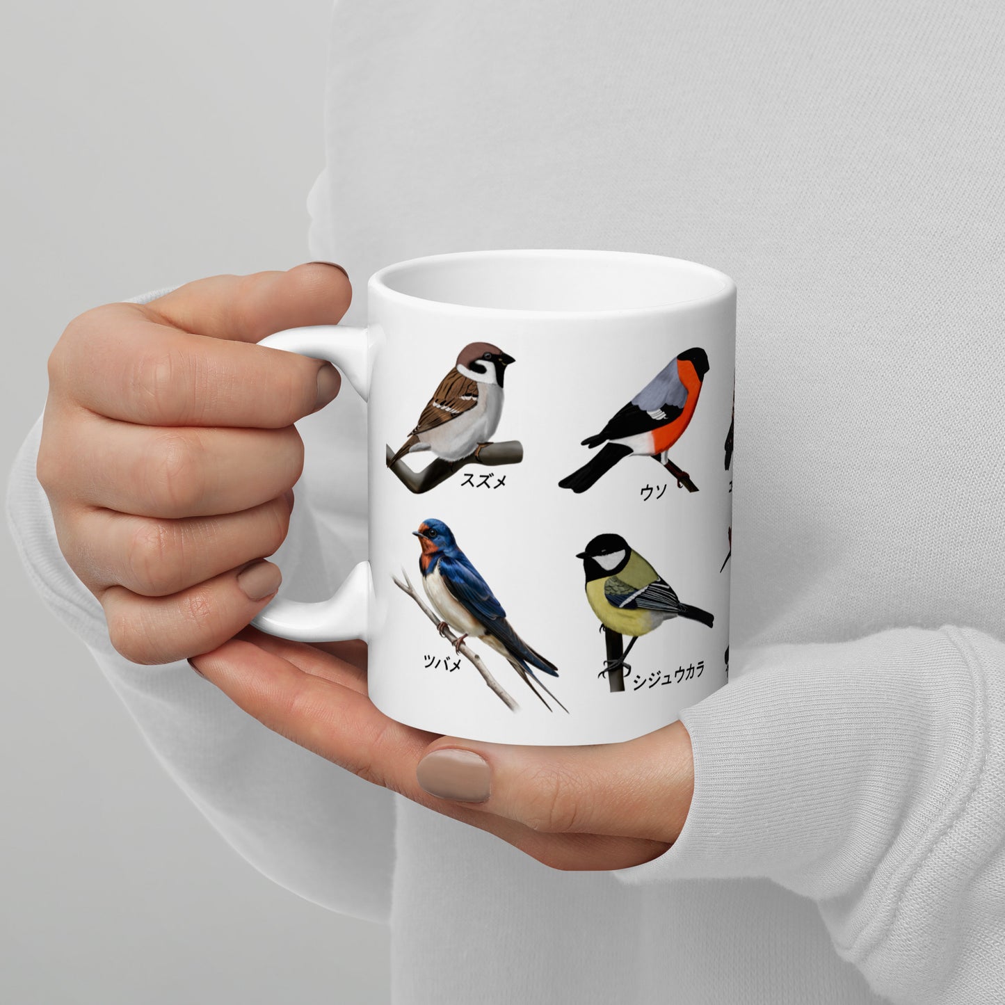 White mug with bird illustrations held by a person against a light gray background